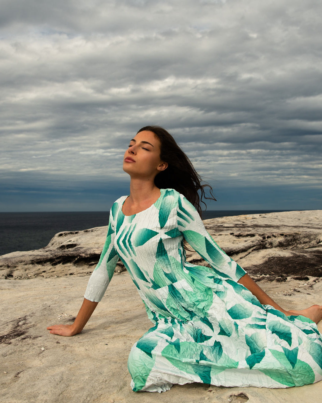 Alquema model in green pleated dress on a rocky coast