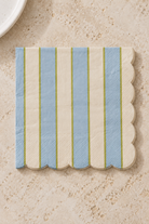 Carnival Paper Napkins - Blue and Ivory in a precisely aligned thin paper stack, viewed overhead on a pale stone bench; Coast to Coast KW5519