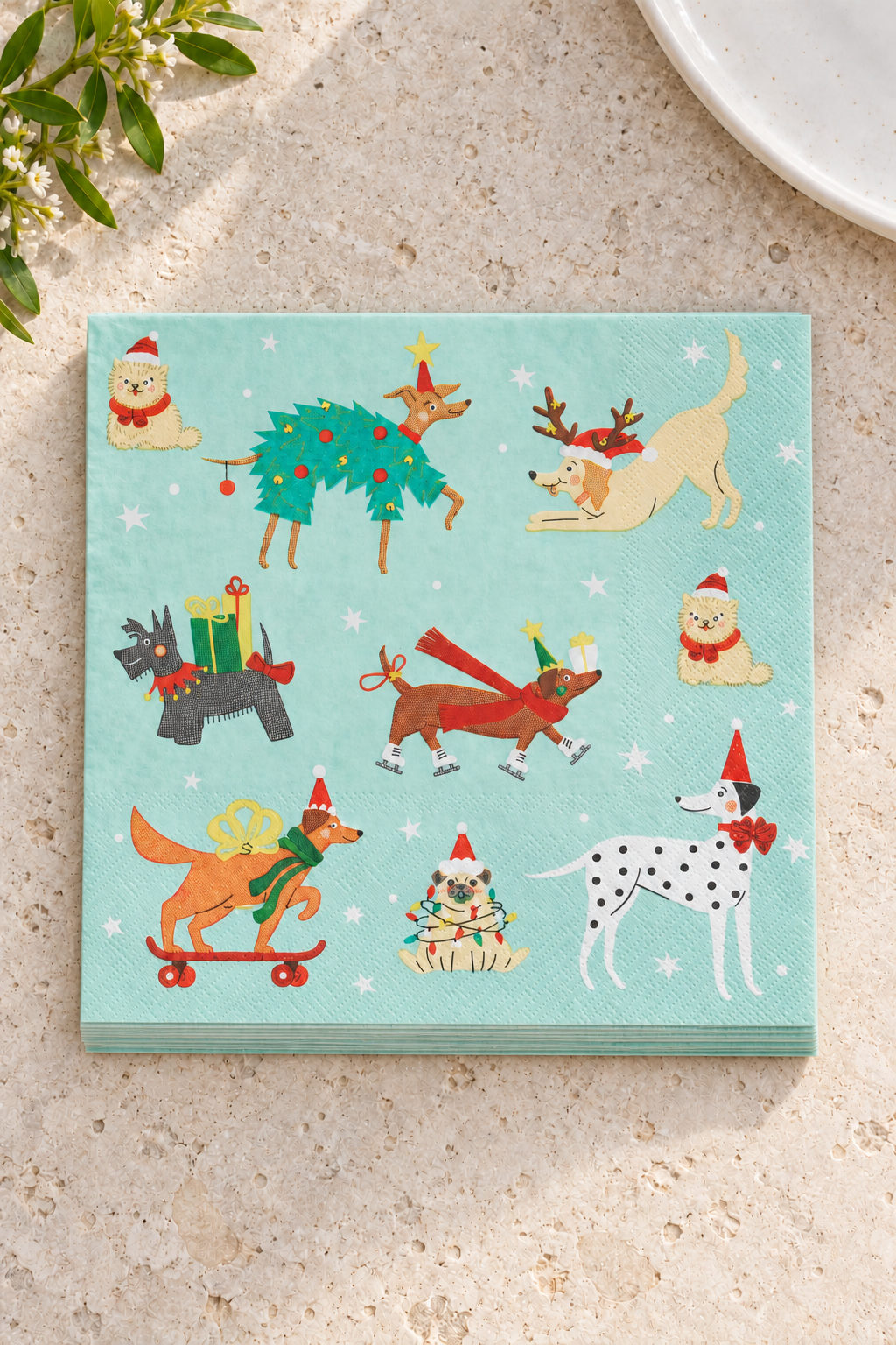 Holiday Dogs Paper Napkins in a precisely aligned thin paper stack, viewed overhead on a pale stone bench; Coast to Coast XM2408