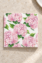 Hydrangea Paper Napkins - Pink in a precisely aligned thin paper stack, viewed overhead on a pale stone bench; Coast to Coast KW5357