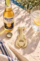 Gold lobster bottle opener styled with a chilled Corona in a coastal setting