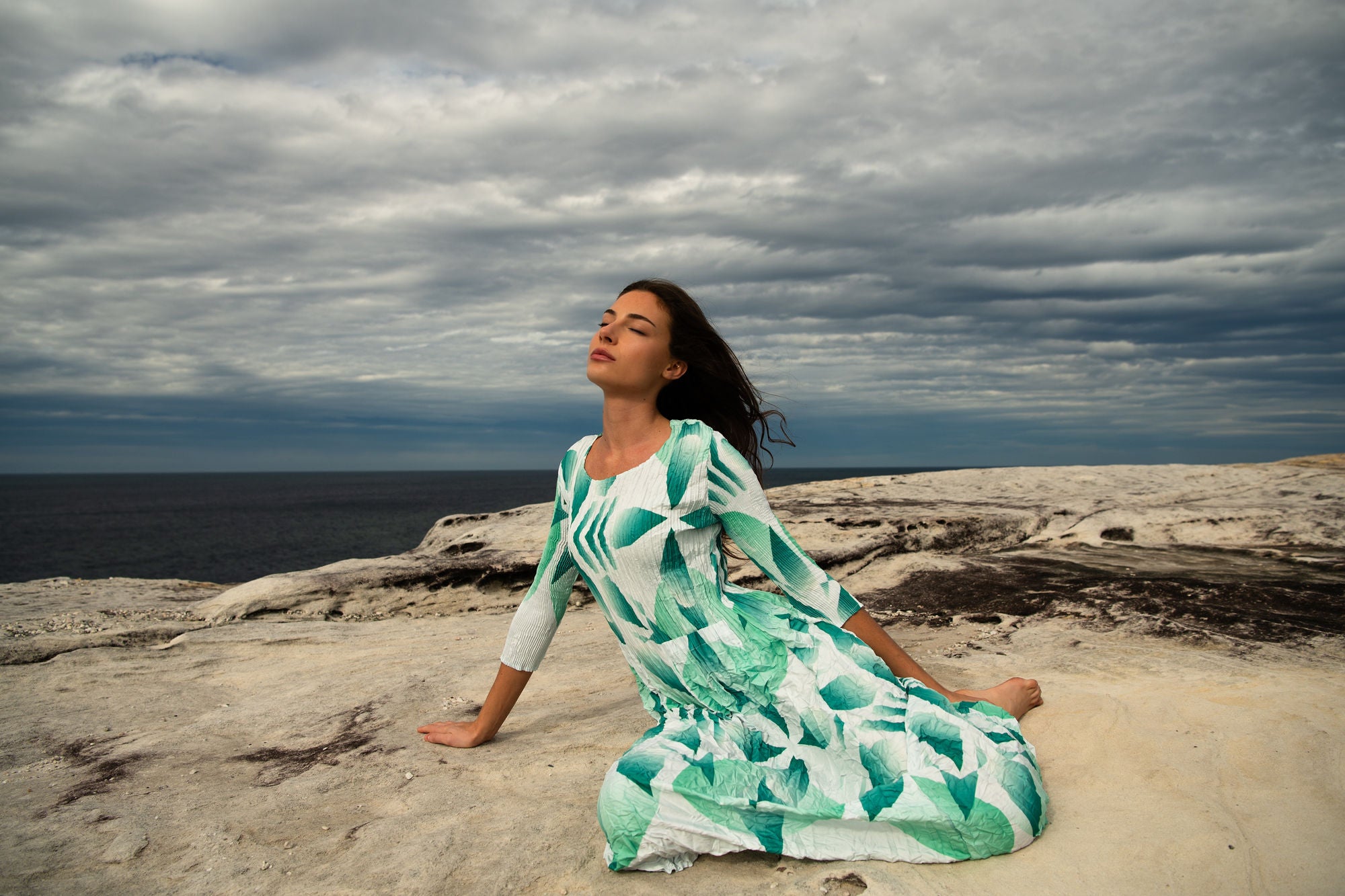 Alquema model in green pleated dress on a rocky coast